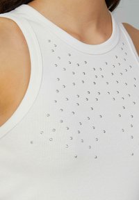 Witte geribbelde tanktop met een hoge halslijn, voorzien van zilveren rhinestone accenten die in een stippenpatroon op de voorkant zijn geplaatst.