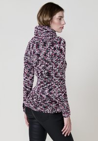 Pull en tricot dans des teintes de rose, blanc et noir. Présente un col haut et une silhouette ajustée. Motif texturé sur l'ensemble, manches longues.