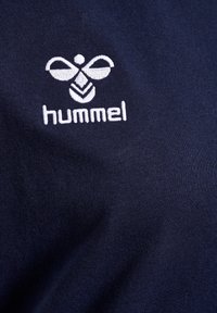 Marineblå bomullsskjorte med hvit brodert "hummel"-logo og tilhørende grafisk design. Glatt tekstur med subtil stretch.