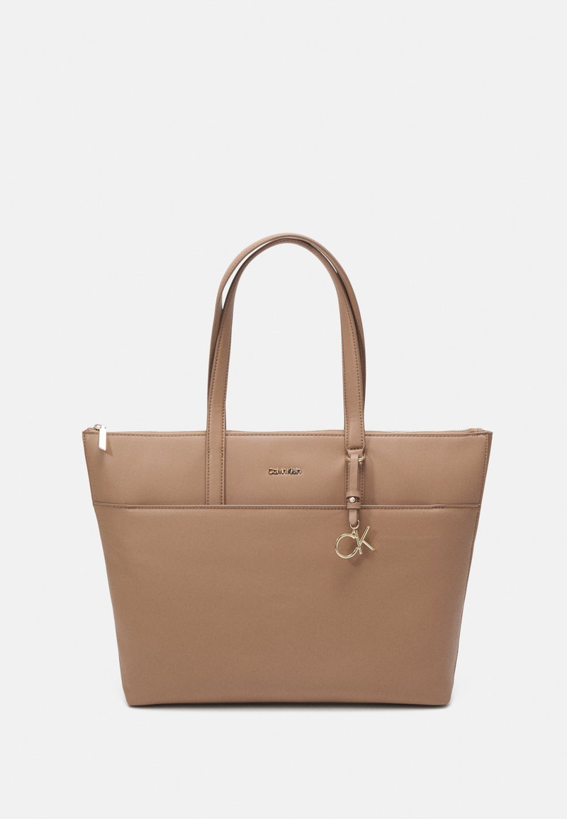 Braune Leder-Umhängetasche mit zwei Griffen, glatter Oberfläche, Reißverschluss und Logo-Detail in goldfarbener Ausführung. Mit einem kleinen Charm versehen.