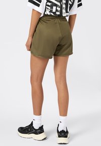 Pantaloni sportivi verde oliva realizzati in tessuto testurizzato, con vita elastica e design a metà coscia. Sono indossate sneakers nere.