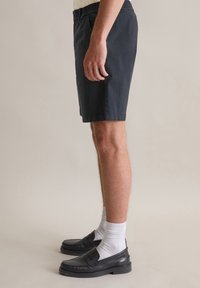 Marineblauwe shorts van katoen met een elastische tailleband. Gecombineerd met zwarte leren instappers en witte crew-sokken.