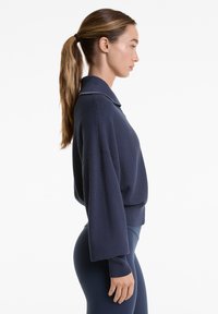 Navyblaue Langarm-Sweatshirt mit strukturiertem Design, Kragen und weiten Ärmeln, kombiniert mit figurbetonten navyblauen Leggings.