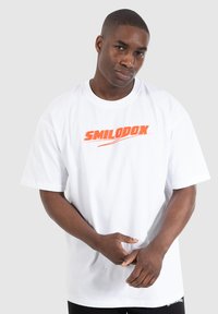 Hvid bomulds t-shirt med et iøjnefaldende orange "SMILODOX" logo på brystet, korte ærmer og en afslappet pasform.