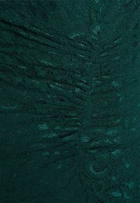 Tissu en dentelle de couleur vert foncé avec des motifs floraux et de feuilles texturés. Présente une finition douce et délicate ainsi que des détails complexes tout au long.