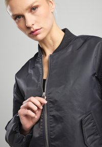 Black bomber jacket with a smooth, shiny finish; features a zip front, ribbed cuffs, and a stand collar; designed with side pockets.