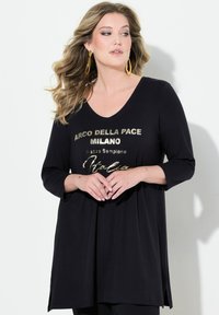 Zwarte lange mouwen tuniek met een V-hals en gouden bedrukte tekst: "ARCO DELLA PACE MILANO Piazza Sempione Italia." Zacht materiaal, losse pasvorm.