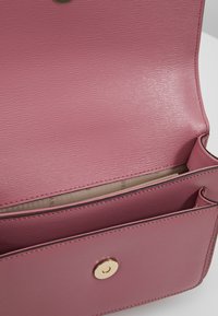 Borsa a mano in pelle rosa con superficie texturizzata. Presenta una chiusura a scatto in ottone e una tasca interna, con una fodera in tessuto liscio.