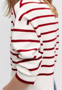 Pull en tricot avec des rayures horizontales rouges sur un fond crème, doté d'une coupe décontractée et de manches retroussées.