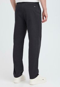 Dark gray trousers made of cotton, featuring a straight-leg design, side pockets, and a back patch pocket with subtle branding.