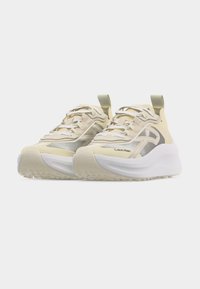 Ζευγάρι μπεζ και λευκά αθλητικά παπούτσια Calvin Klein με παχιά σόλα και κορδόνια, σε απλό ανοιχτό γκρι φόντο.