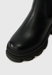 Μαύρο δερμάτινο μποτάκι αστραγάλου με στρογγυλή μύτη, υφασματική σόλα από λάστιχο και χαρακτηριστικό σχέδιο βάσης. Λείος φινίρισμ�α με ελάχιστες λεπτομέρειες.