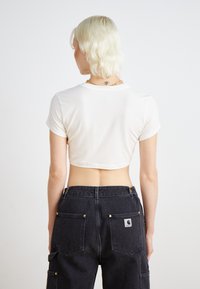 Bílý crop top s krátkými rukávy, kombinovaný s černými cargo kalhotami s zlatými kovovými detaily a zadními kapsami. Hladká textura látky.
