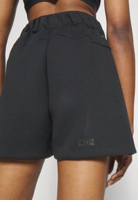 Shorts de sport noirs avec une taille élastiquée, une texture lisse et un logo discret imprimé sur l'ourlet inférieur. Présente une coupe décontractée.
