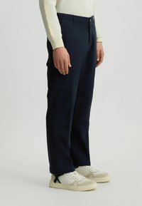 Marine cargobroek met meerdere zakken, een rechte pasvorm, gemaakt van stof met een gladde textuur. G gedragen met witte sneakers en een lichte top.