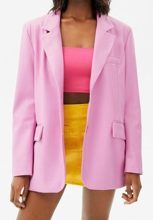 Femme portant un blazer rose pastel, un top tube rose vif et une mini-jupe jaune taille haute, vue de la mi-cuisse au cou.