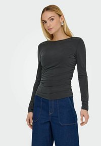 Langærmet, mørkegrå top med samlet tekstur ved taljen, parret med højtaljede blå denimbukser. Enkel halsudskæring og tæt siddende ærmer.