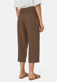 Bruine, cropped broeken met een smocked tailleband, die een textuurstof en een relaxte pasvorm tonen. Geëxposeerd vanaf de achterkant met sandalen.
