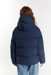 Jachetă puffer bleumarin cu glugă, cu un design matlasat și un finisaj mat. Spatele prezintă o siluetă aerodinamică și cusături rezistente.