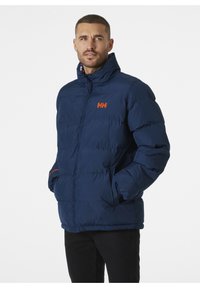 Chaqueta acolchada azul marino con logo naranja, cuello alto y cierre frontal con cremallera. Presenta puños de canalé y bolsillos laterales para mayor calidez y estilo.