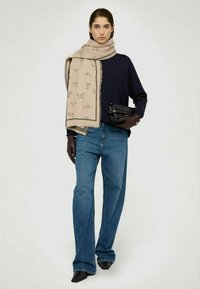 Beige mønstret tørklæde, navy blå langærmet skjorte, udvidede blå jeans, sorte læderhandsker og mørke spidse sko. Enkel, moderne design.