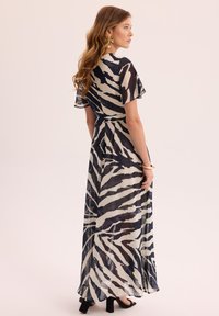 Maxi sukienka z przezroczystego materiału, ozdobiona granatowo-kremowym wzorem w zebra. Posiada krótkie falbany na rękawach, dopasowaną talię i zwiewny krój.