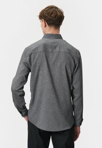 Grijze button-up shirt in een geweven textuur met lange mouwen en een gebogen zoom, voorzien van een standaard kraag en zwarte knopen op de manchetten.