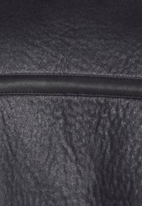 Svart texturerat läder med en slät svart dragkedjeakcent längst upp. Ytan visar ett distinkt, veckat mönster.