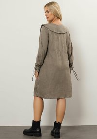 Brun och krämfärgad houndstooth-klänning med stor krage, långa ärmar och knutna manschetter, kombinerad med svarta ankelstövlar.