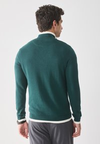 Pulover verde tricotat cu mâneci lungi și accente albe cu jumări la guler și la tiv. Designul are o croială standard și o textură netedă.