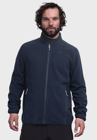 Navy fleece jacket with a high collar, full zip, side pockets, and a minimalist logo on the chest. Soft texture and relaxed fit.