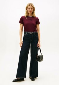 Bordeaux bomulds t-shirt med hvid udskæring, sammen med brede mørke denimbukser. En sort håndtaske og flade sko fuldender outfittet.