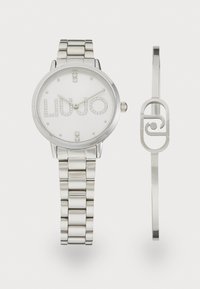 Zilveren roestvrijstalen horloge met een witte wijzerplaat, met de inscriptie "LIU JO" in stenen en een gebandeerde armband. Inclusief een minimalistische armband.