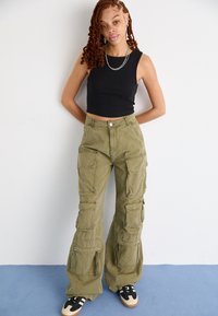 Olijfgroene katoenen cargopants met meerdere zakken, hoge taille en een ontspannen pasvorm. Gekenmerkt door een zwart mouwloos topje en sneakers.