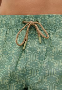 Shorts de bain verts avec un motif floral et de vagues, un cordon de serrage marron, une taille élastique et un tissu texturé.