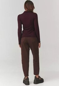 Burgundowa bluzka z długim rękawem połączona z brązowymi spodniami o tapered kroju. Teksturowany materiał i dopasowany krój z gładkim wykończeniem oraz widocznymi detalami przeszycia.