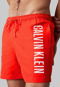 Bañador rojo confeccionado en un tejido ligero que cuenta con una cintura elástica con cordón ajustable y un gran texto blanco "CALVIN KLEIN" en el lateral.