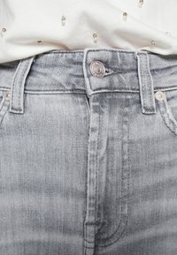 Světlé šedé džíny z denimu s těsným střihem, pěticípým stylem kapes a zapínáním na knoflík se stříbrným kováním.