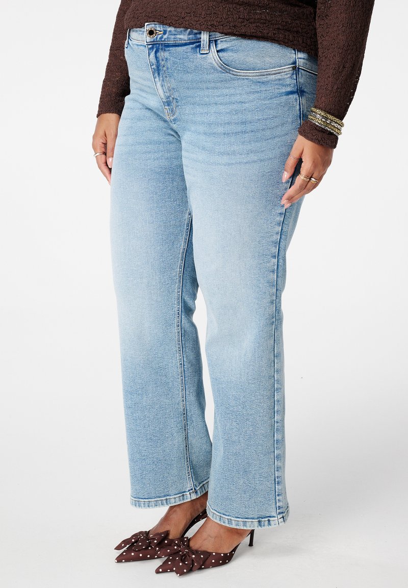 Lichtblauwe rechte jeans met een lichte vervaging, voorzien van vijf zakken, riemlussen en gestikte zomen. Gecombineerd met bruine hakken met polkadots.