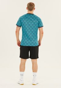 Turkis atletisk T-shirt med et struktureret gittermønster, sorte accenter, parret med sorte shorts. Model med ryggen til, stående på en neutral baggrund.