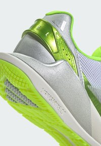 High-performance sneaker featuring a silver upper with green accents, textured material, and a patterned rubber sole with prominent grip.