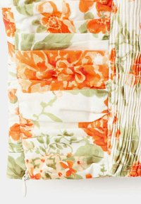Tissu matelassé avec imprimé floral orange et vert et tirette de fermeture éclair blanche visible en bas à gauche.