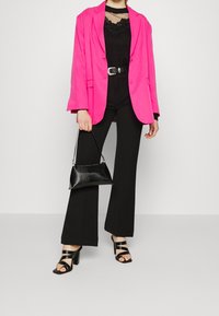 Růžový blazer, černý krajkový top, černé rozšířené kalhoty, černé sandály na vysokém podpatku a malá černá kabelka. Tkanina je hladká s různými texturami.