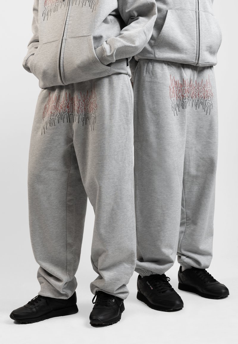 Grijze katoenen hoodie en sweatpants met een rood en zwart vlamgrafiek op de voorkant. Draagt met zwarte veterschoenen.