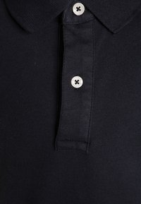 Námořnická polo košile s jemnou strukturou, klasickým límcem a stříbrnými knoflíky s logem. Tkanina se zdá být prodyšná a strukturovaná.