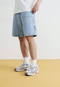 Jeansshorts i lys blå med en avslappet passform og sidelommer, kombinert med hvite ankelsokker og multikolor sneakers.