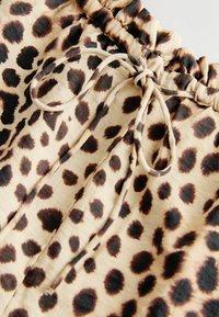 Gros plan sur un tissu beige à imprimé léopard brun foncé, avec une ceinture élastique et un cordon de serrage noué.