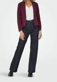 Blazer bordeaux sur un haut blanc associé à un jean en denim foncé taille haute. Bottines noires; coupe droite; texture de tissu lisse.