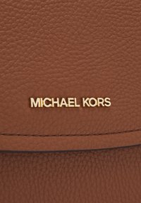 Surface en cuir marron texturée avec des lettres dorées formant le nom de la marque "MICHAEL KORS" fixées près d'une couture.