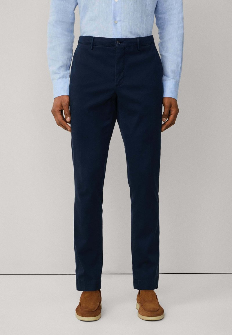 Navy blue chinos made from cotton, featuring a straight fit, zip fly, and button closure. Smooth texture with side pockets and belt loops.